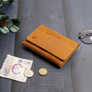 The yellow trifold wallet placed on a table with a few coins and a banknote, emphasizing its functionality for carrying both cash and cards in a compact design.