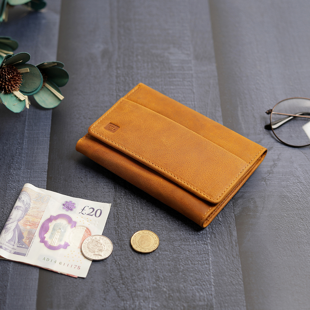 The yellow trifold wallet placed on a table with a few coins and a banknote, emphasizing its functionality for carrying both cash and cards in a compact design.