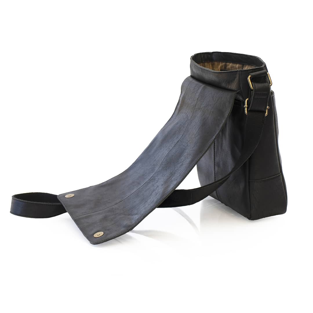 side view of a small black messenger bag. the bag is open to show a flap over closure with magnetic buttons