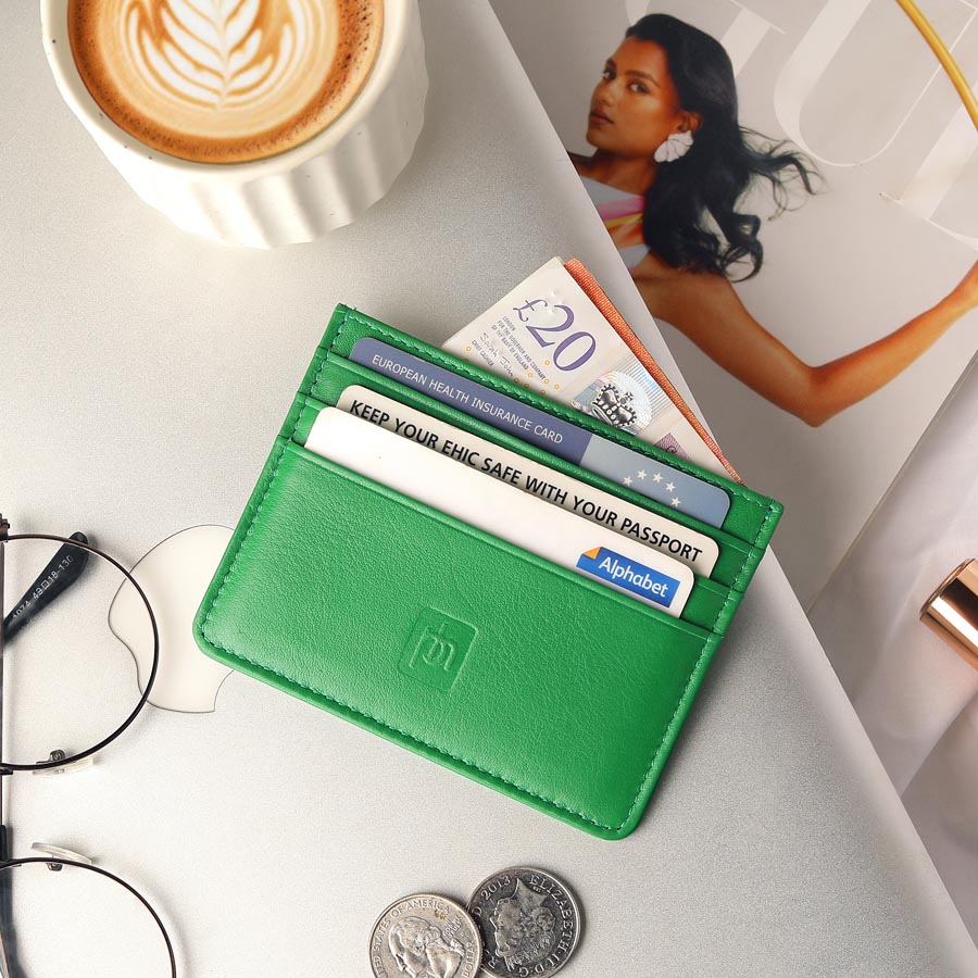 Green Personalised Leather Card Holder with RFID 04 Green leather card holder with cards and cash on a desk beside coffee and glasses
