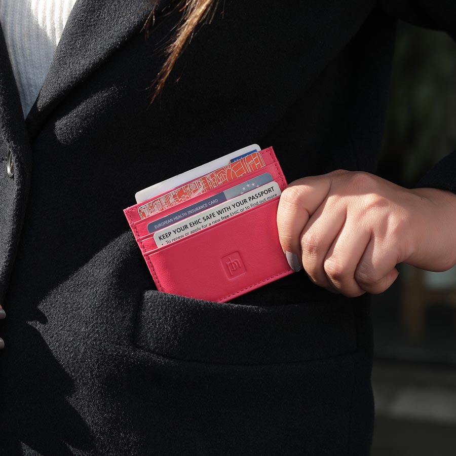 Person placing a pink leather card holder into their coat pocket