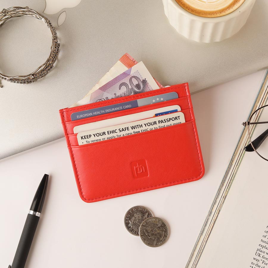 Red leather card holder with cash and cards on a white desk with accessories