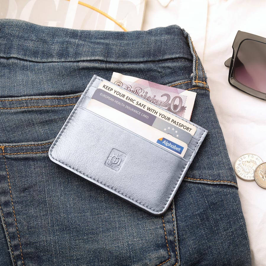 Silver Personalised Leather Card Holder with RFID 01 Silver personalised leather card holder filled with cash and cards, styled on a pair of blue jeans alongside sunglasses and coins.